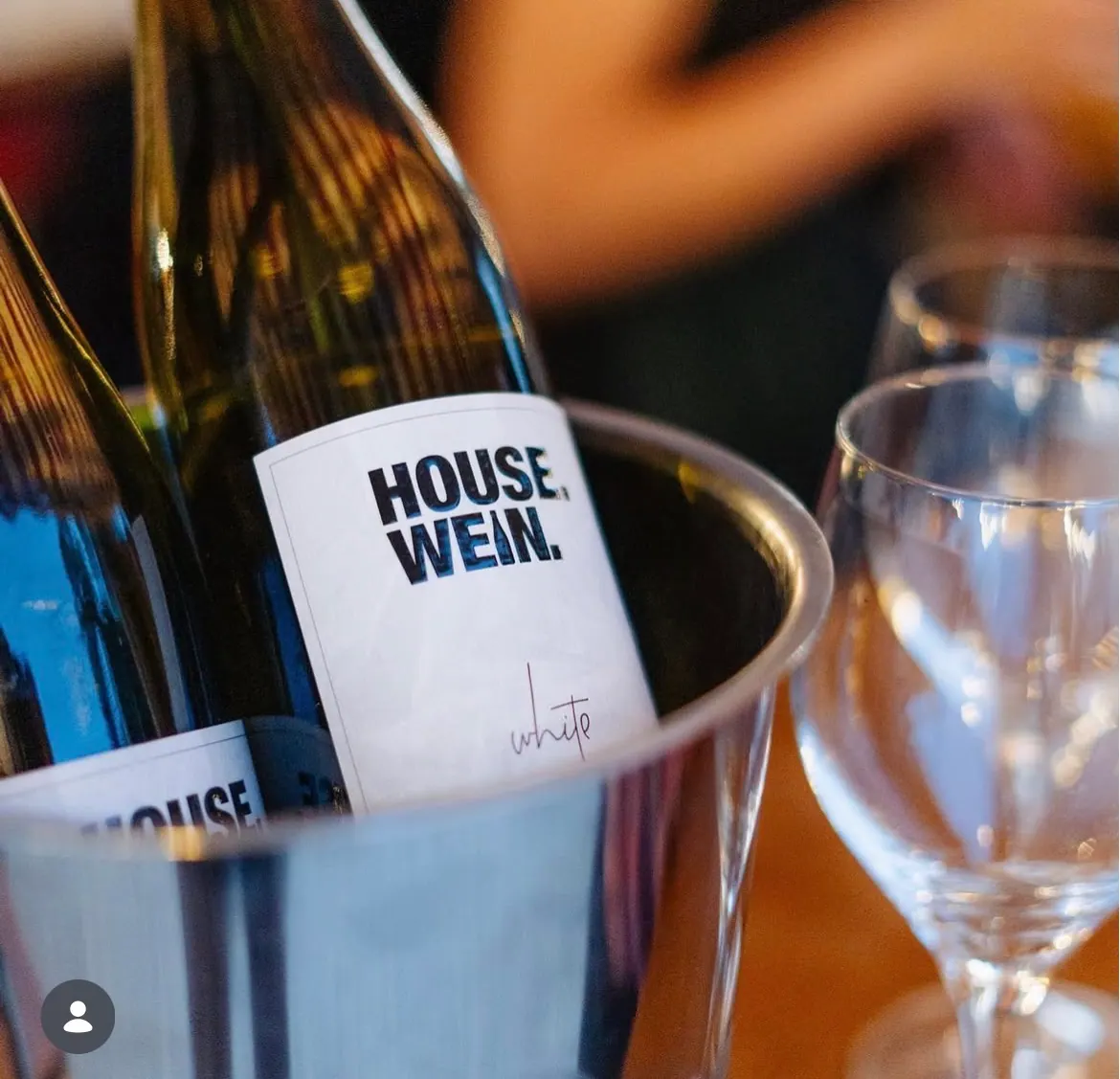 Flasche HOUSE.WEIN. im Weinkühler neben einem Glas